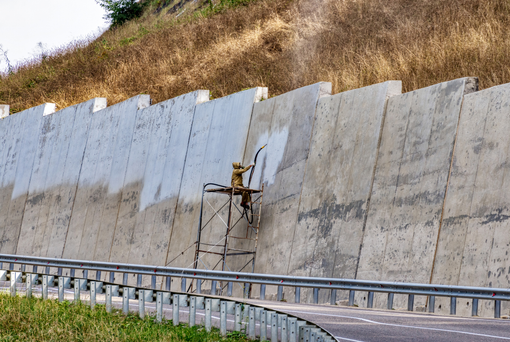 Contact Us A man is painting a concrete wall next to a highway.