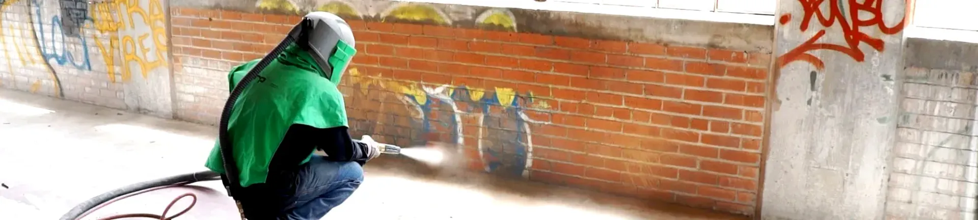 Contact Us A person in a green hoodie is spray painting graffiti on a brick wall.