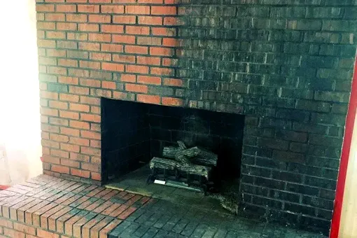 Contact Us A brick fireplace with logs in it in a living room.