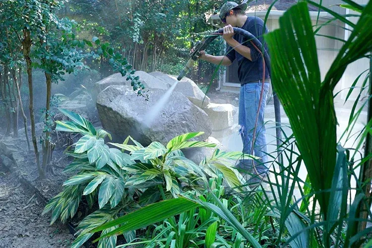 A man is cleaning a large rock with a hose.