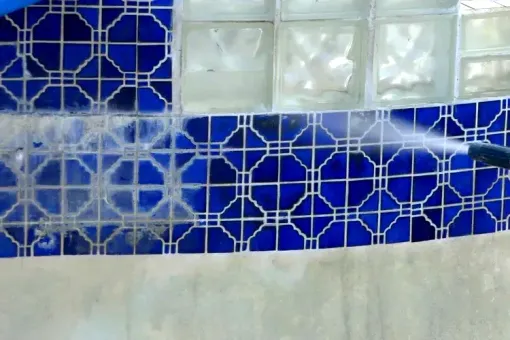 Contact Us A person is cleaning a blue tile wall with a high pressure washer.