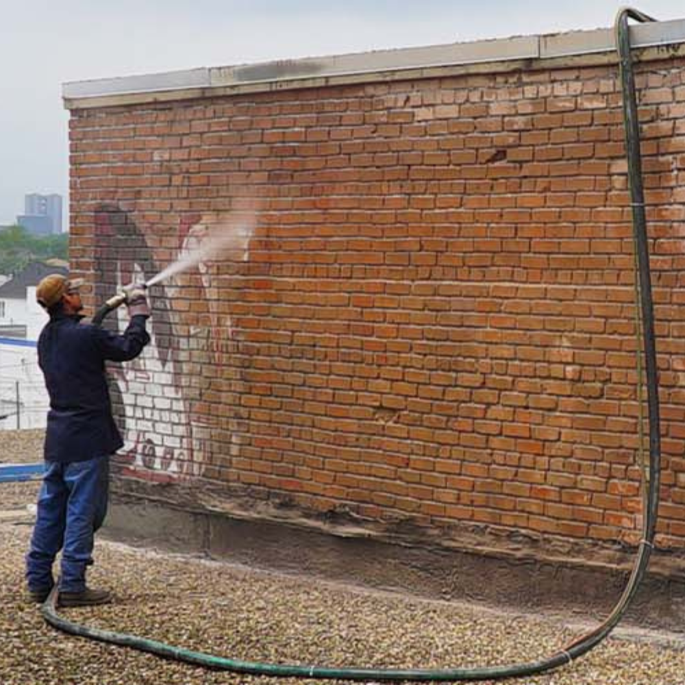 A man is cleaning a brick wall with a hose.