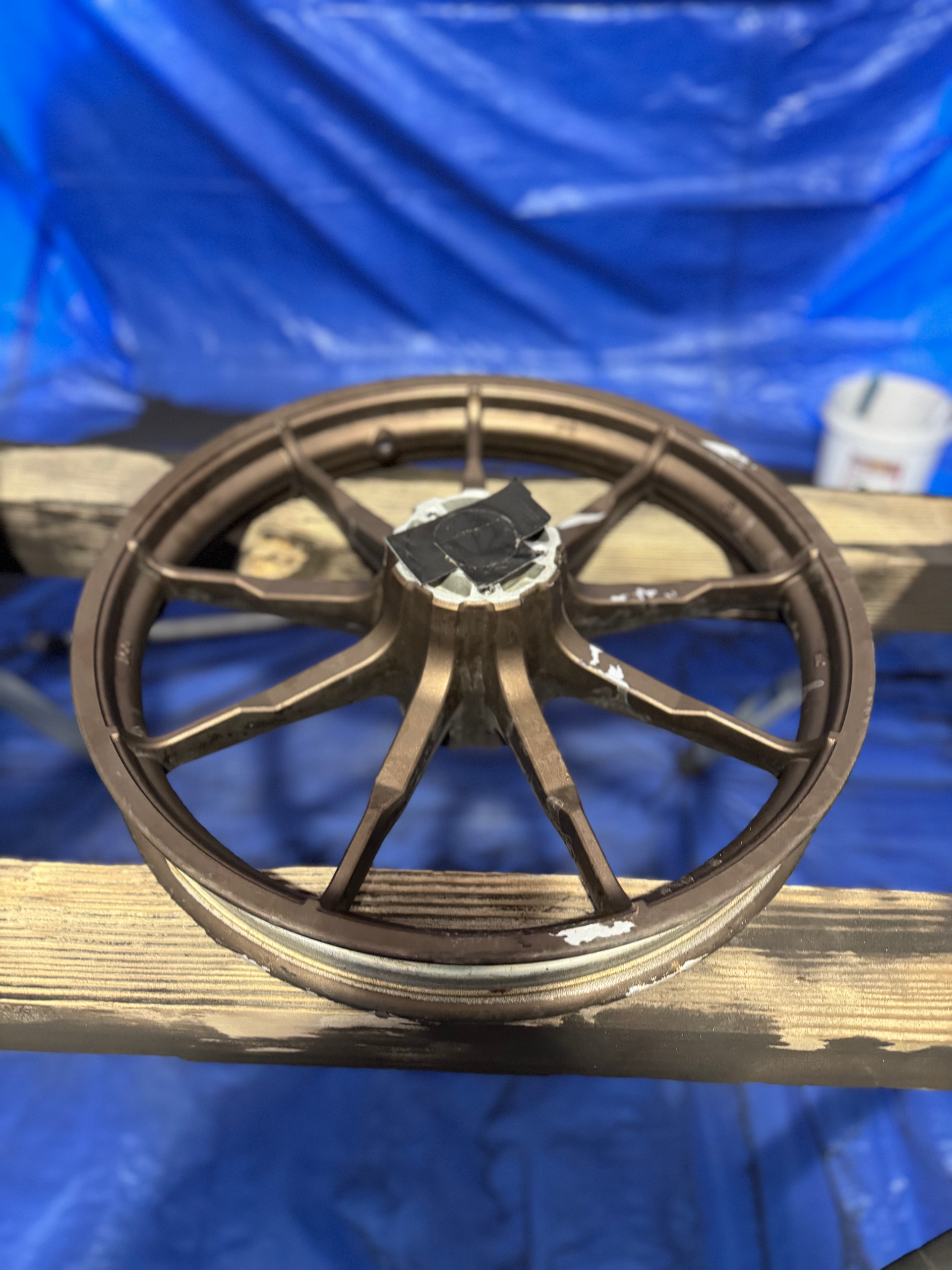 A bicycle wheel is sitting on a wooden shelf in front of a blue tarp.