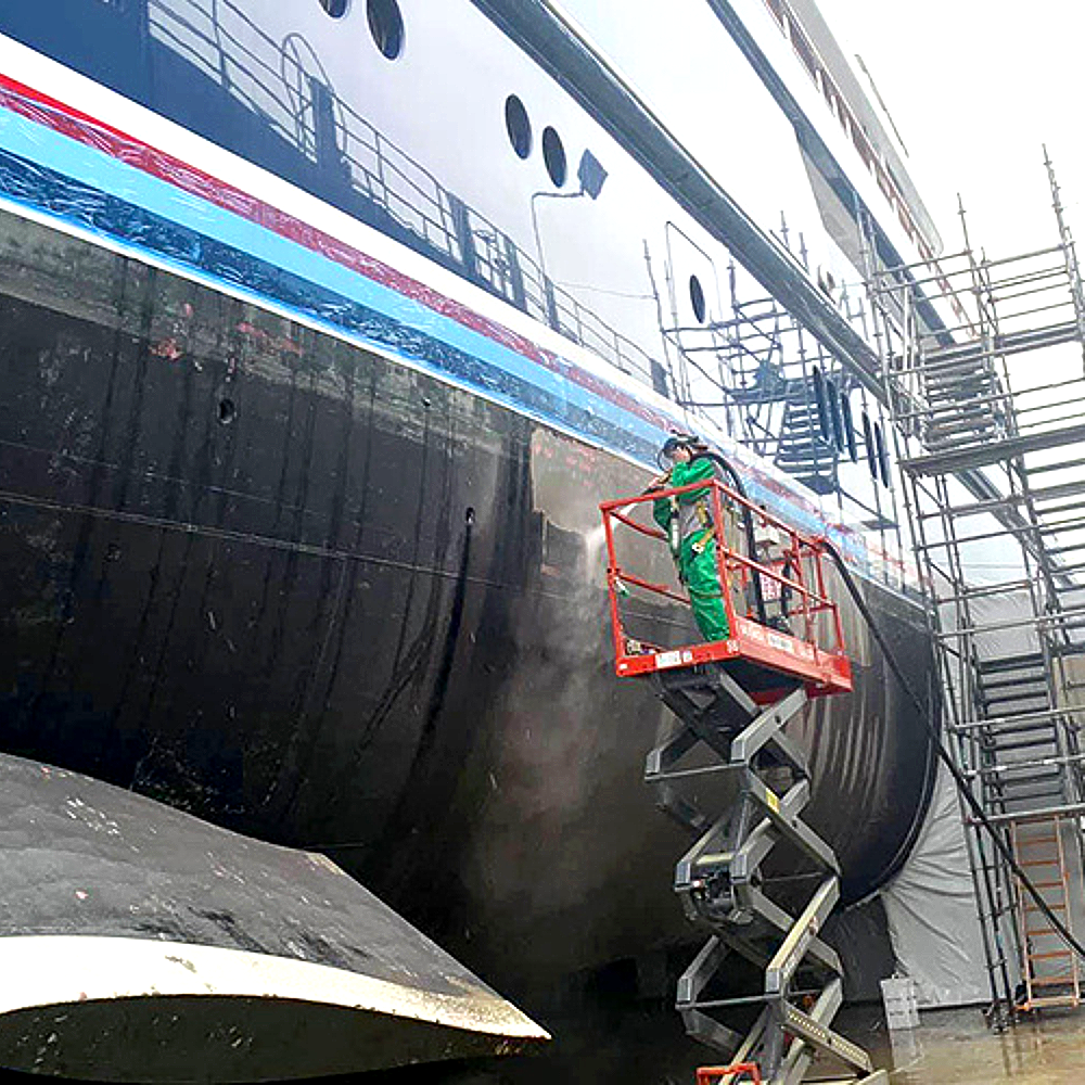 A man is standing on a scissor lift cleaning a large boat.