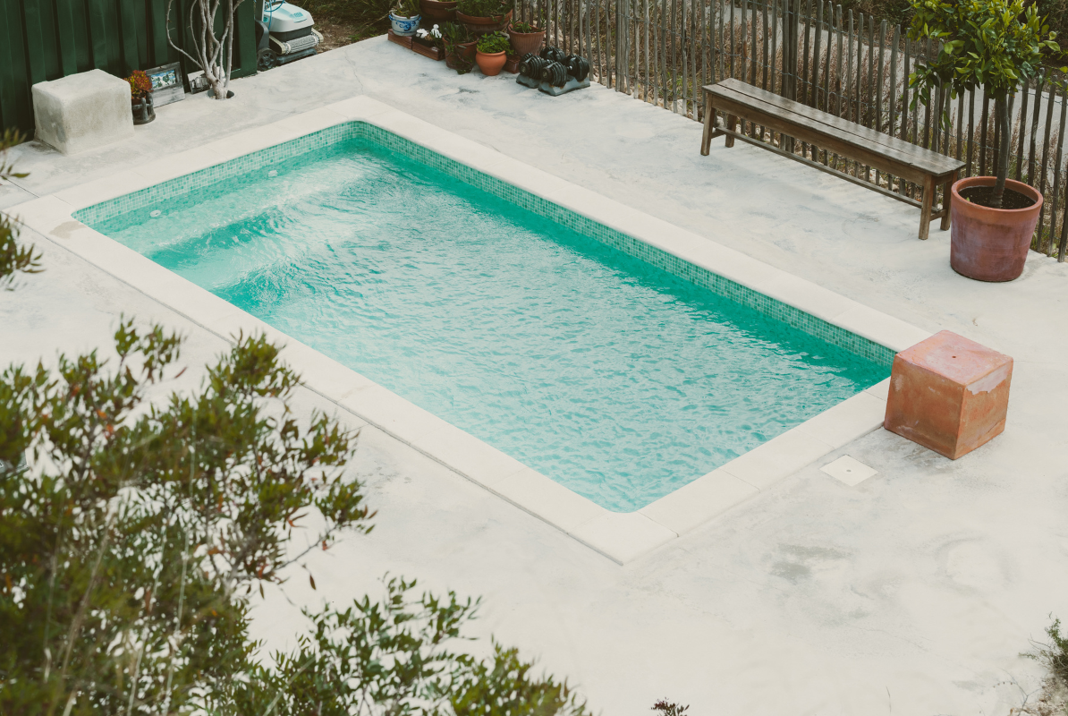 A large swimming pool is surrounded by trees and a bench.