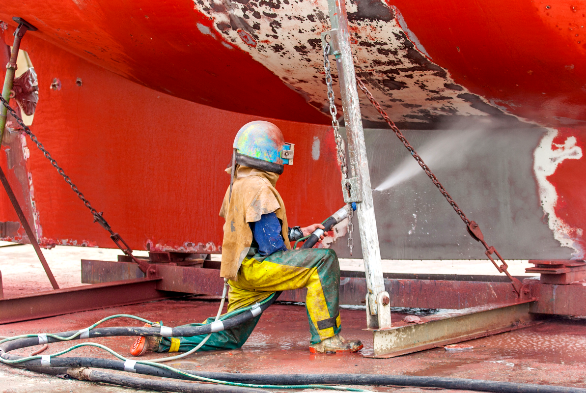 A man is sandblasting the side of a boat.
