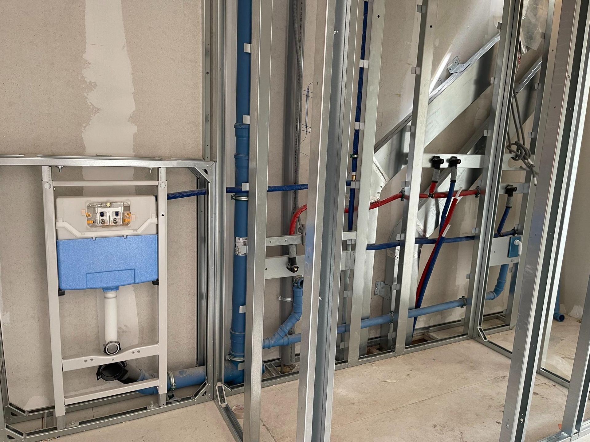 Zichtbare muurconstructie en leidingen in een badkamer die wordt gerenoveerd, inclusief voorbereiding voor een toilet.