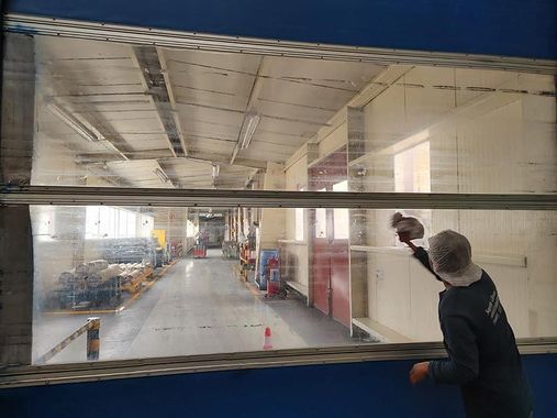 Persona limpiando una ventana grande con vistas al interior de un almacén.