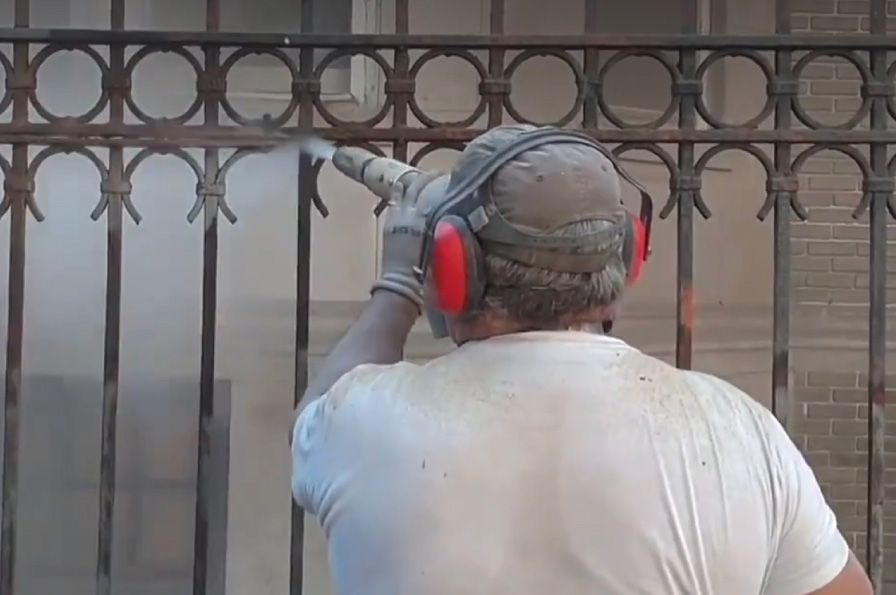 A man wearing ear muffs and headphones is spray painting a wrought iron fence.