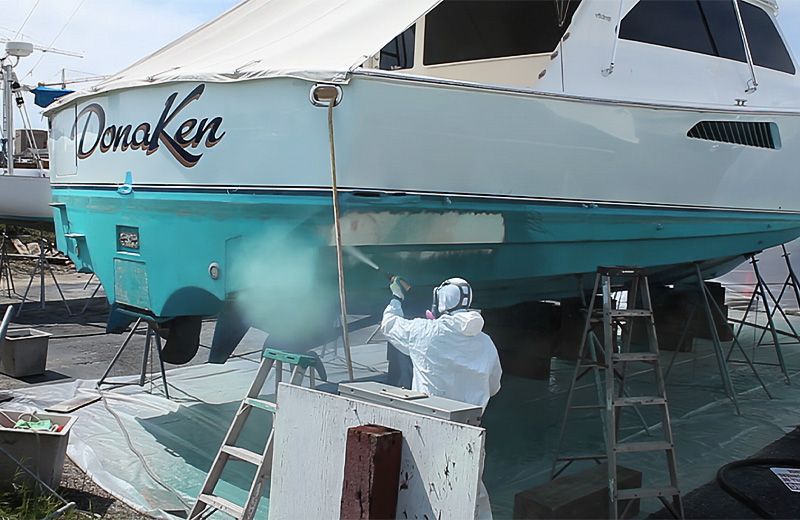 A man in a white suit is spray painting a boat.
