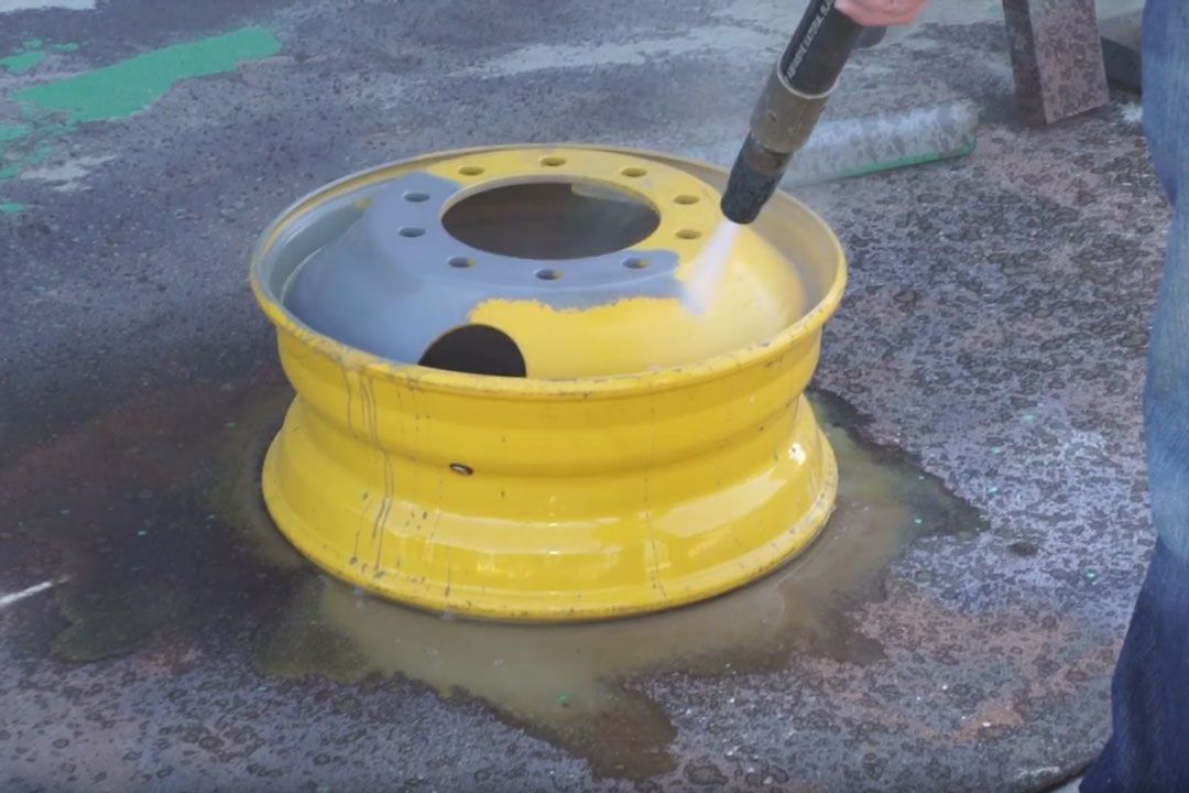 A person is cleaning a yellow wheel with a high pressure washer.