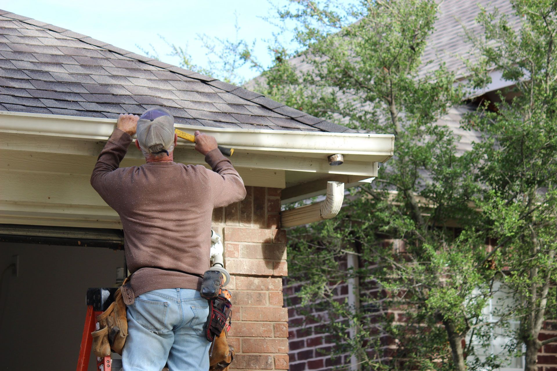 Person on a ladder cleaning a gutter on a brick house.