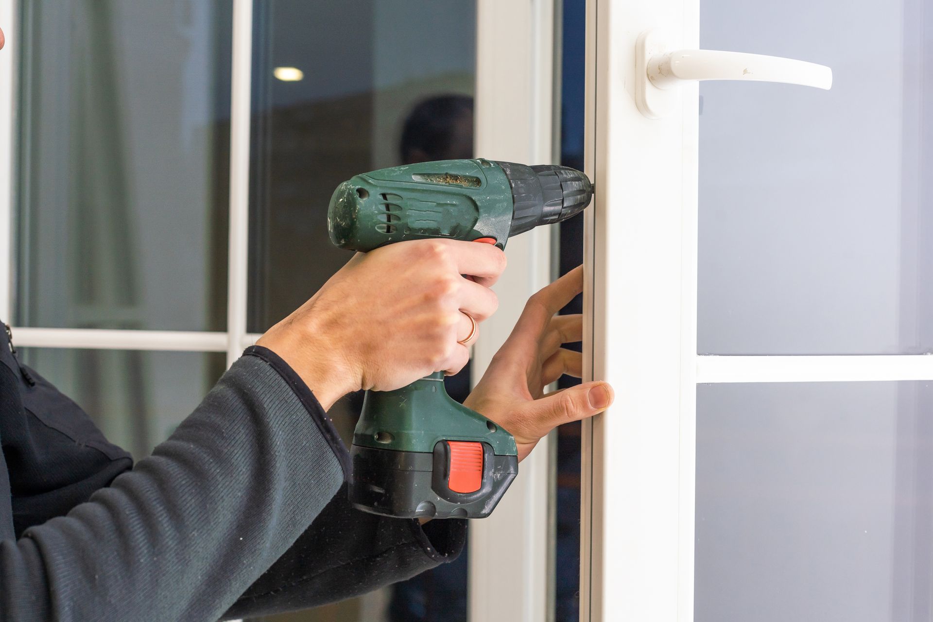 Person using a power drill to work on a white window frame