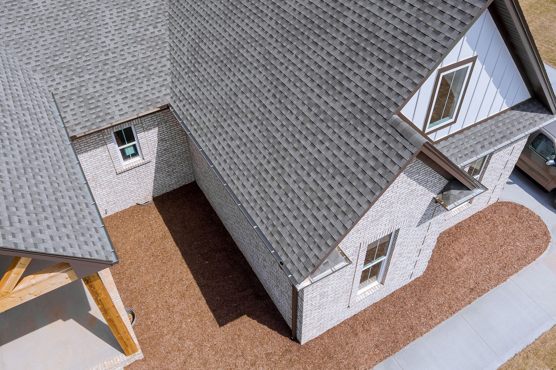High-angle view of a house with gray roof and brick exterior; brown mulch yard and a concrete sidewalk.