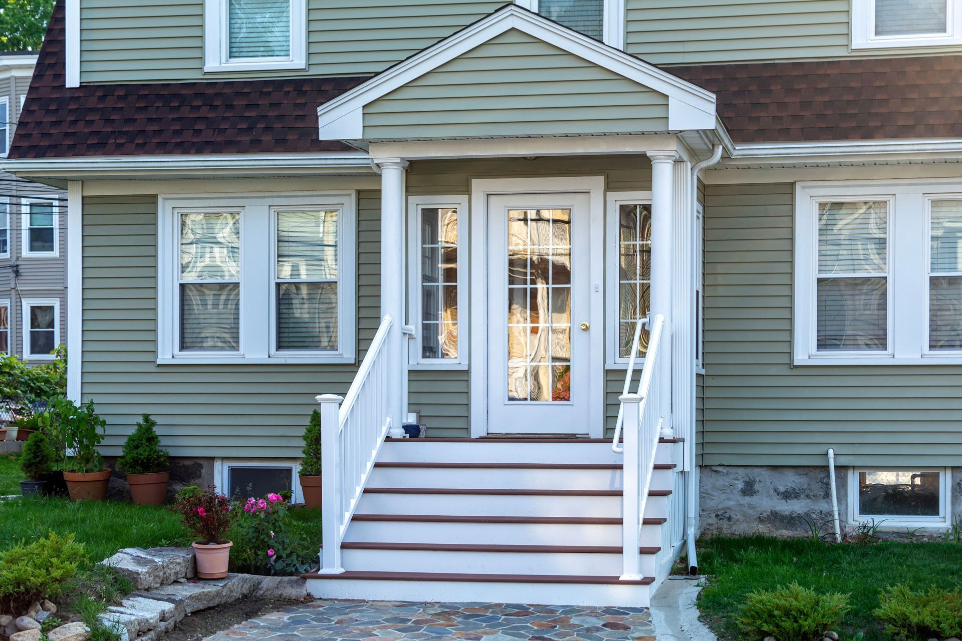 Green house with white trim, front porch with steps and door, windows on either side.