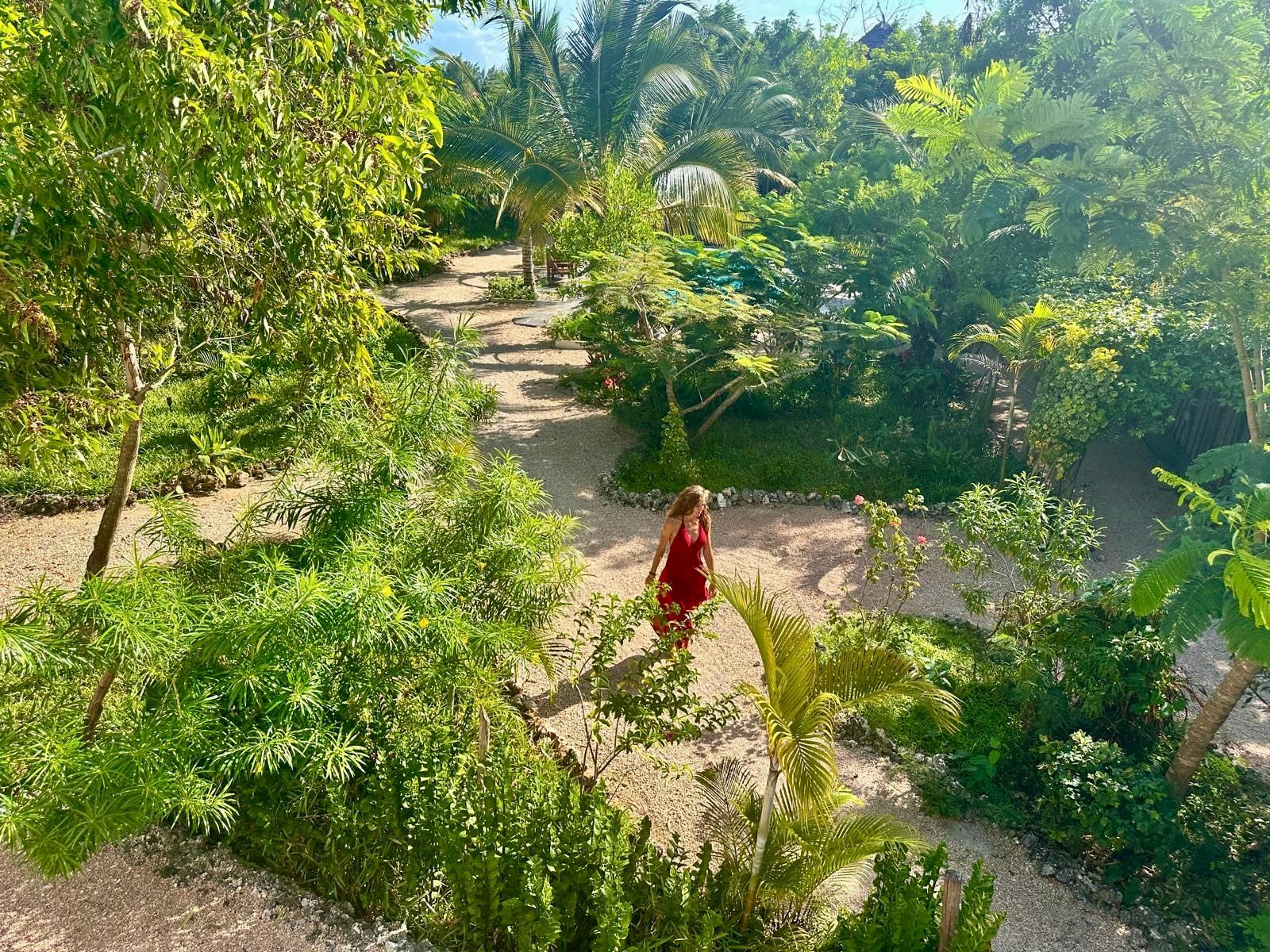 A woman in a red dress is walking through a lush green garden.