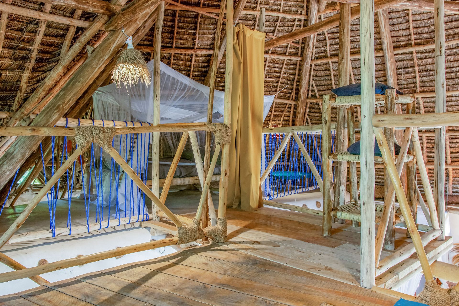 Loft bedroom with thatched roof and wooden railings; blue and white mosquito net visible.