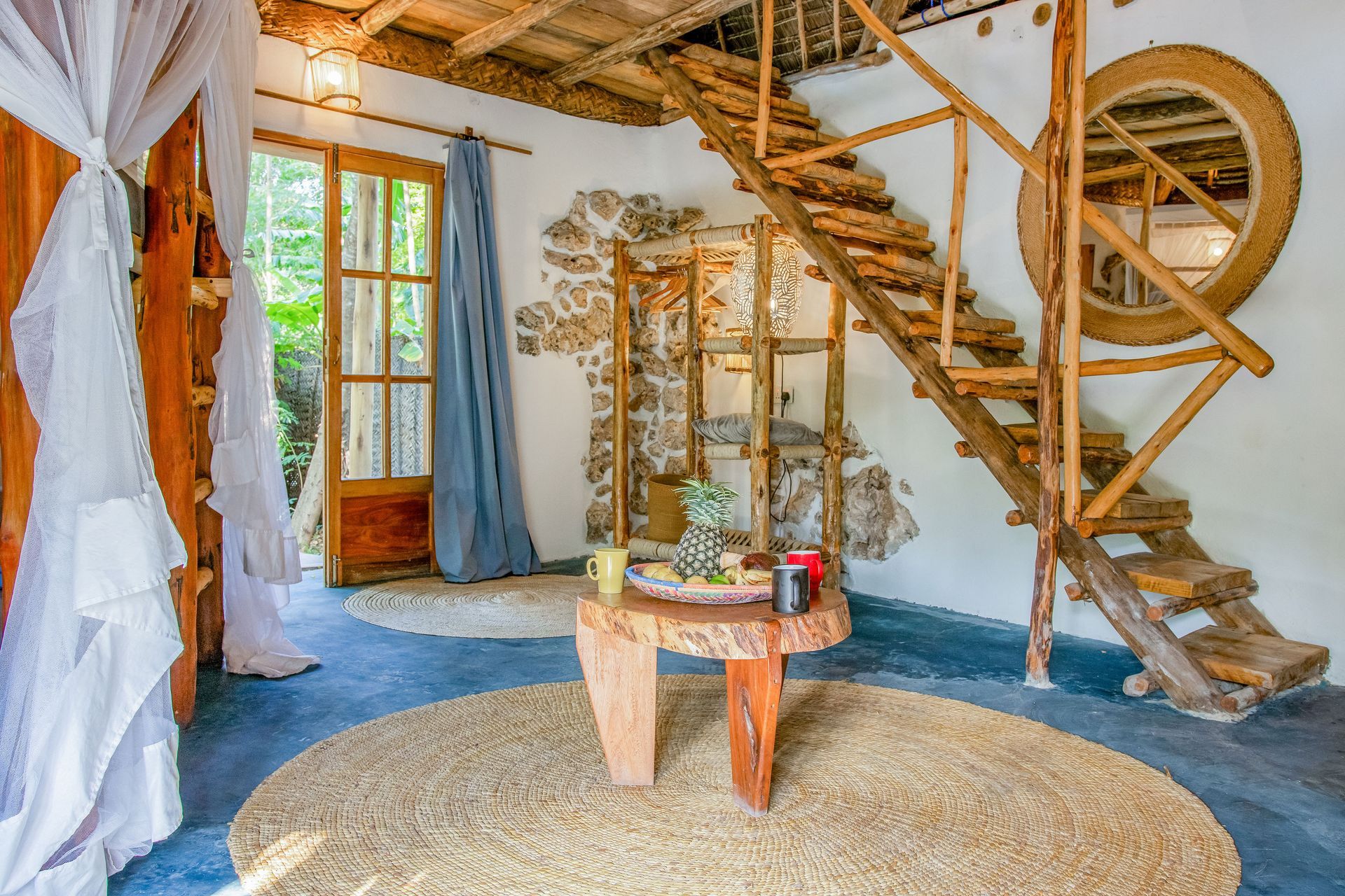 A room with a canopy bed , stairs , a table and a mirror.