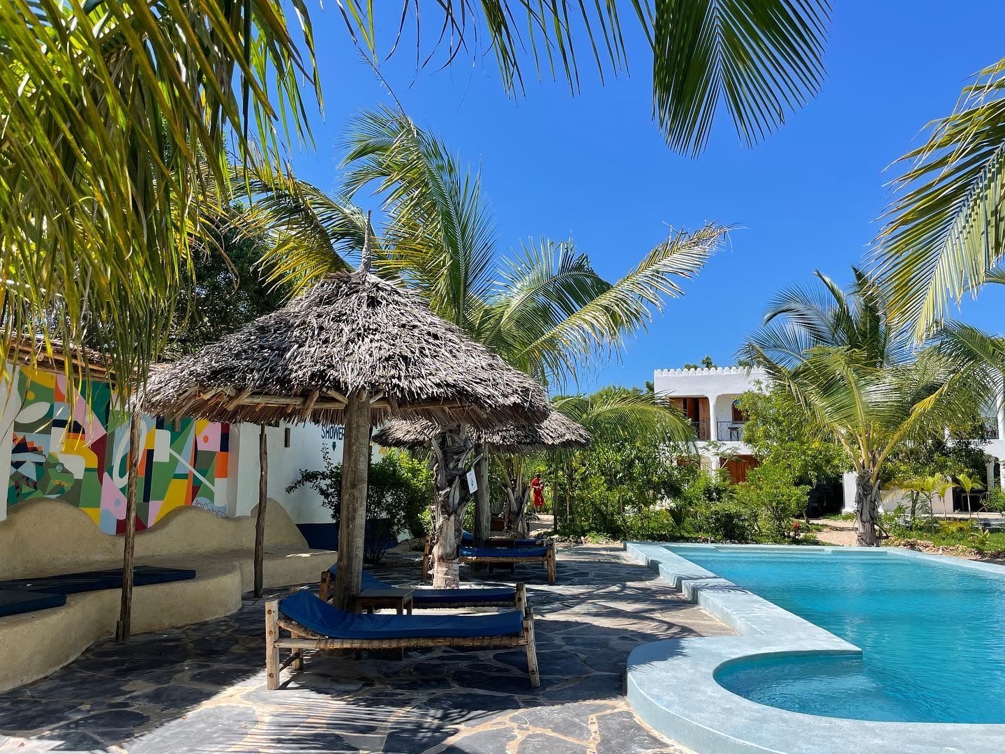 A swimming pool surrounded by palm trees and thatched umbrellas.