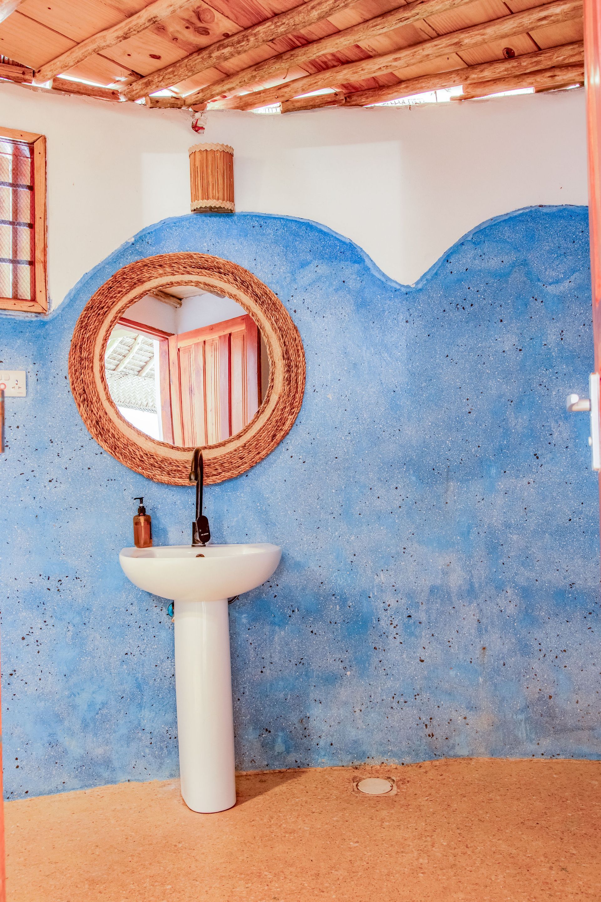 Bathroom with blue textured wall, round mirror, white sink, and terracotta floors and ceiling.