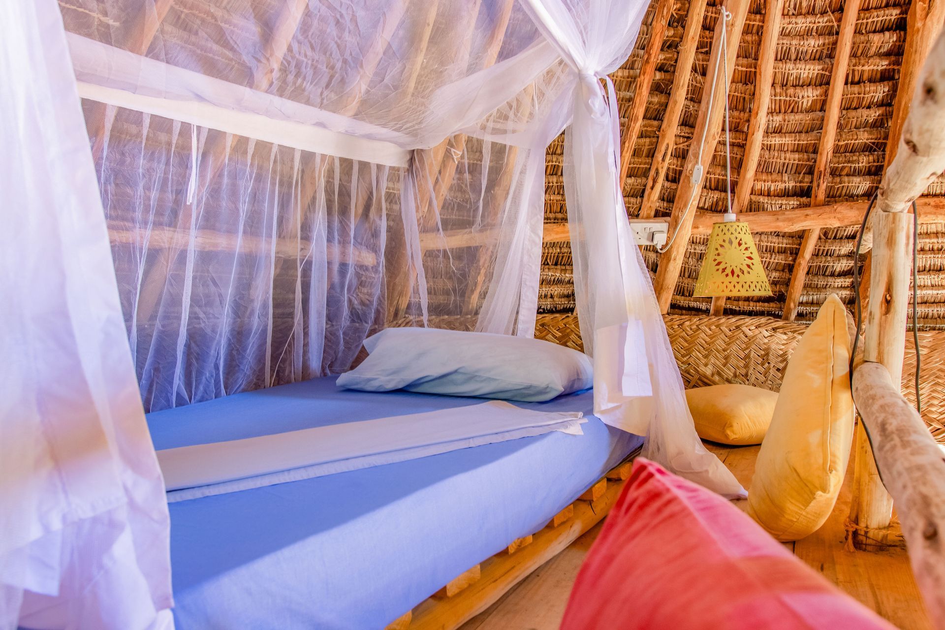 A bed with blue linens and mosquito netting in a rustic room with a thatched roof.