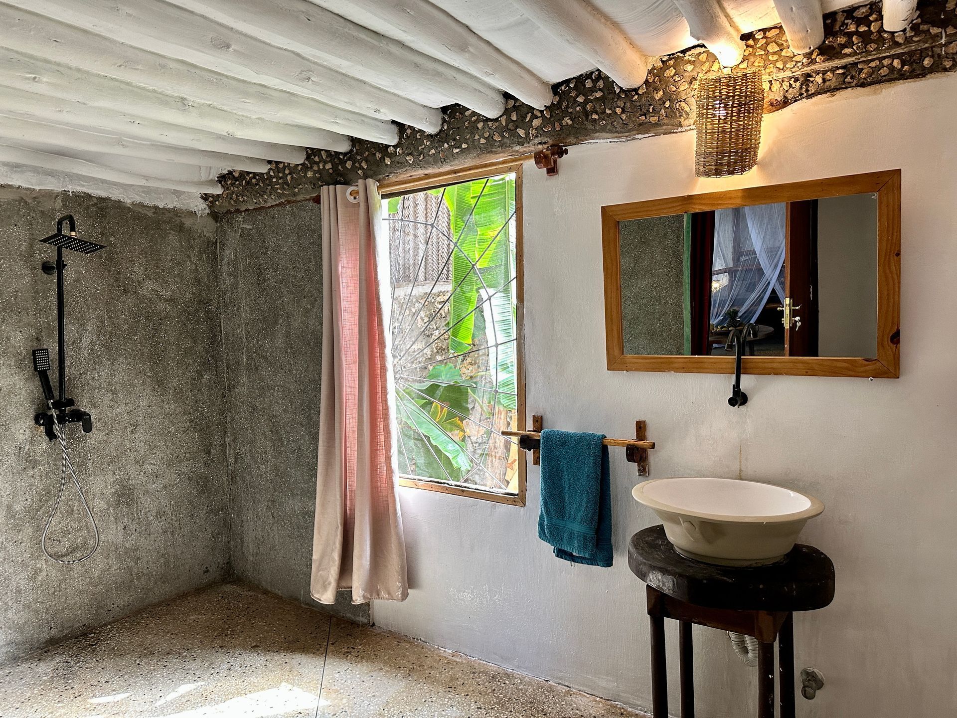 Rustic bathroom with gray shower, window with pink curtain, and sink on a wooden stand.