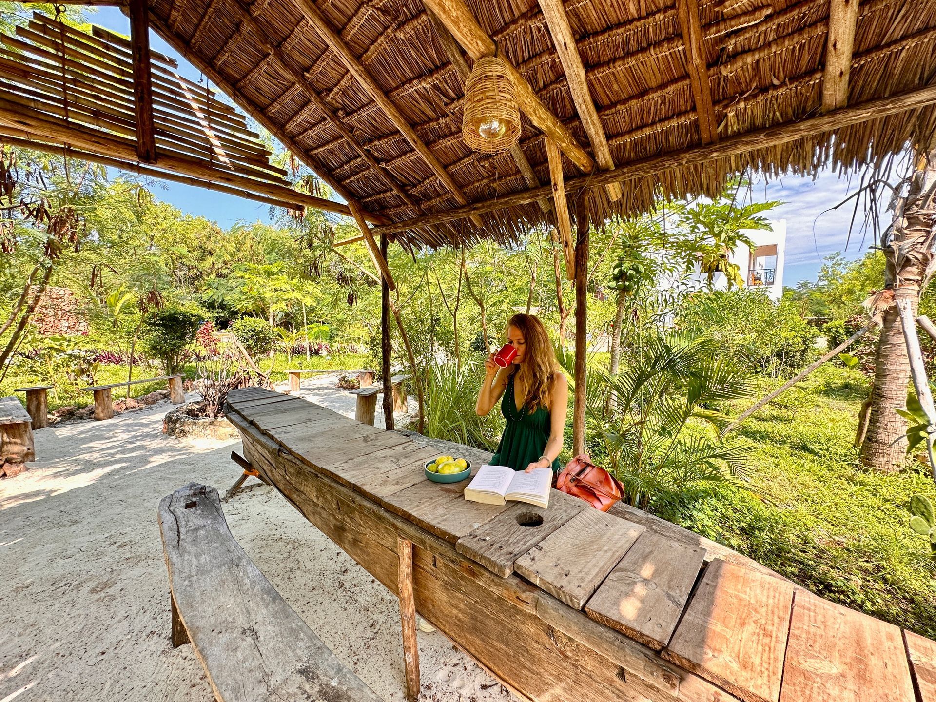 A woman is sitting at a wooden table under a thatched roof.