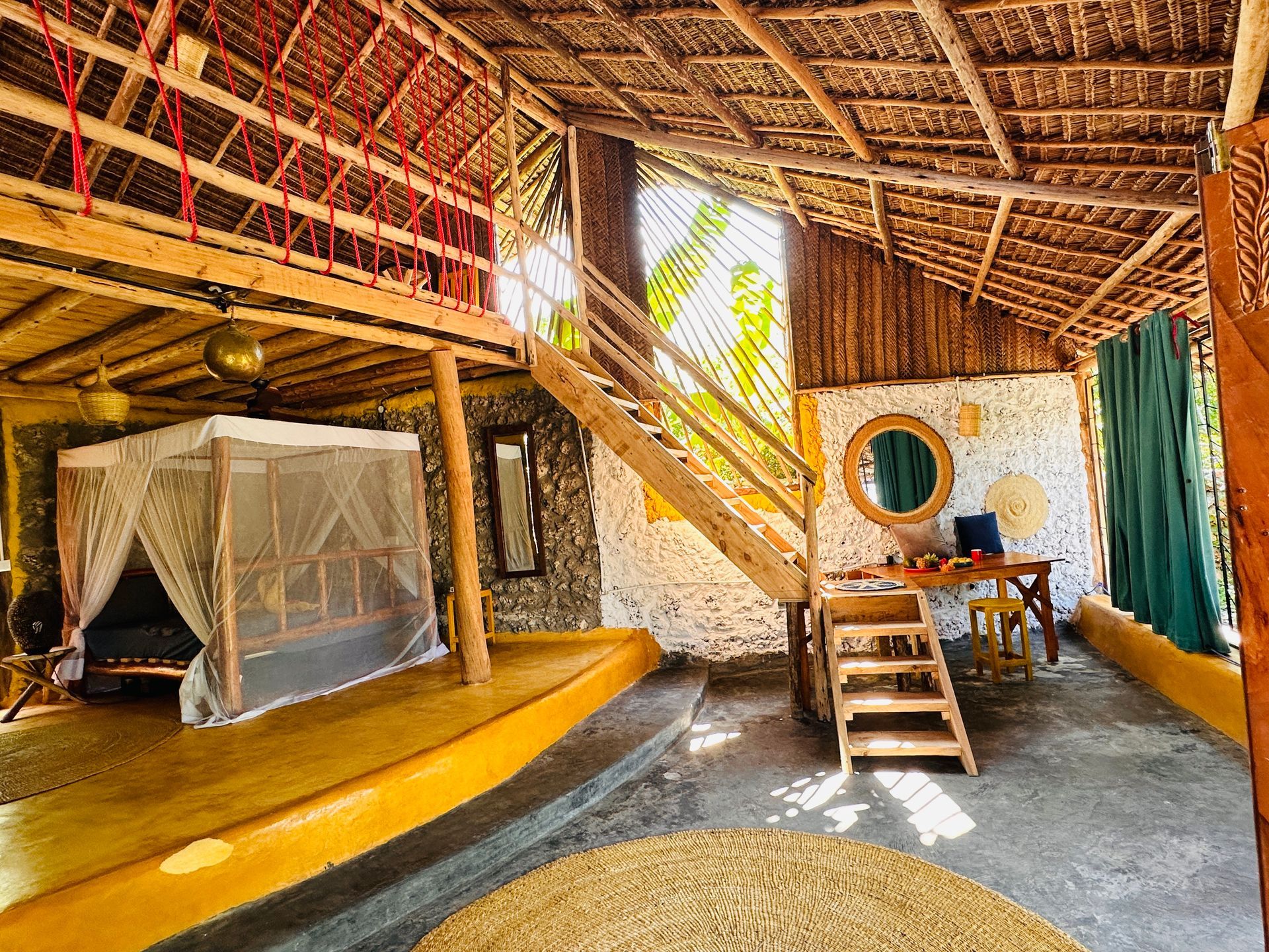 A room with a canopy bed , stairs , a table and a mirror.