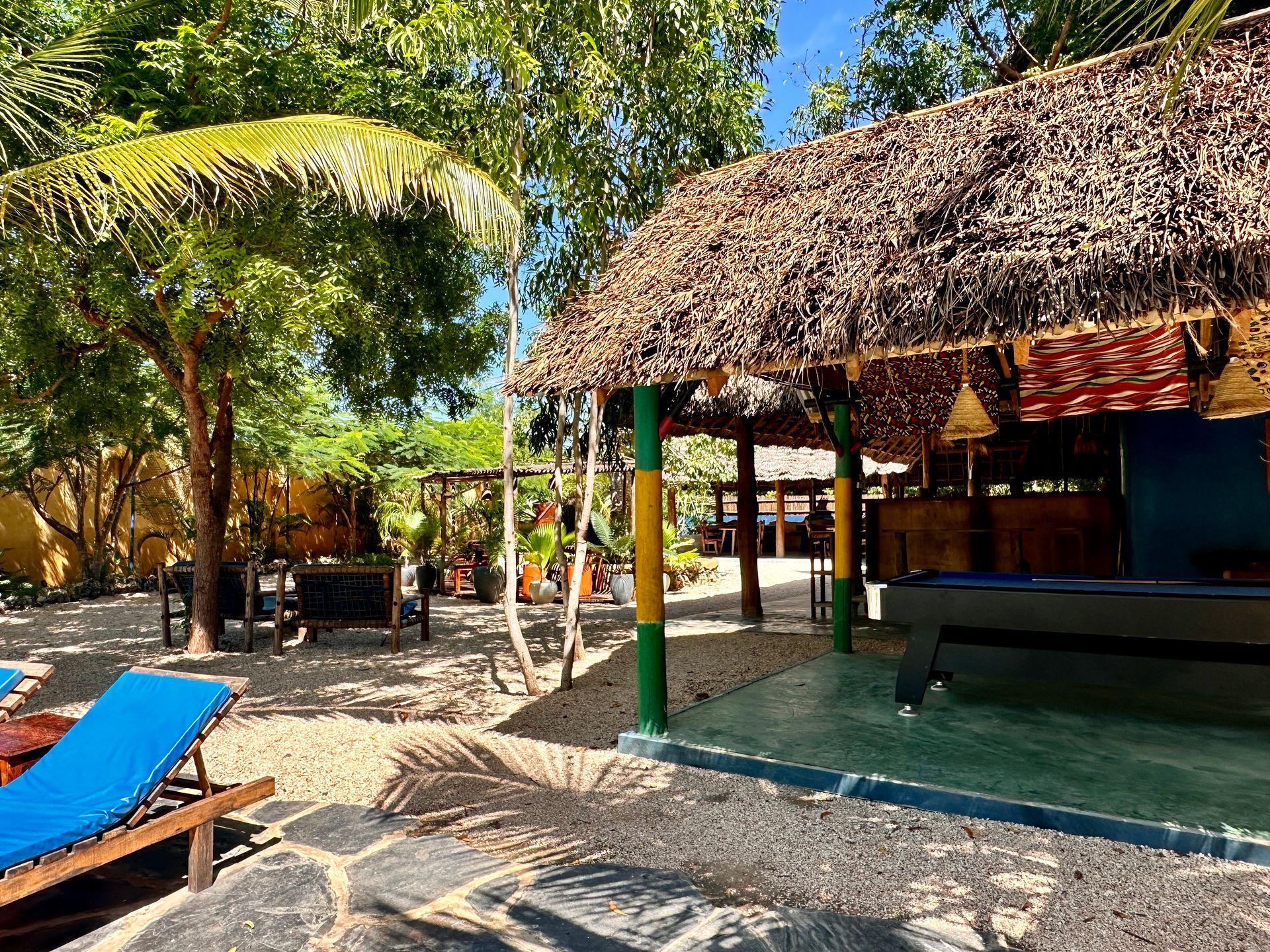 A pool table is sitting under a thatched roof next to a pool.