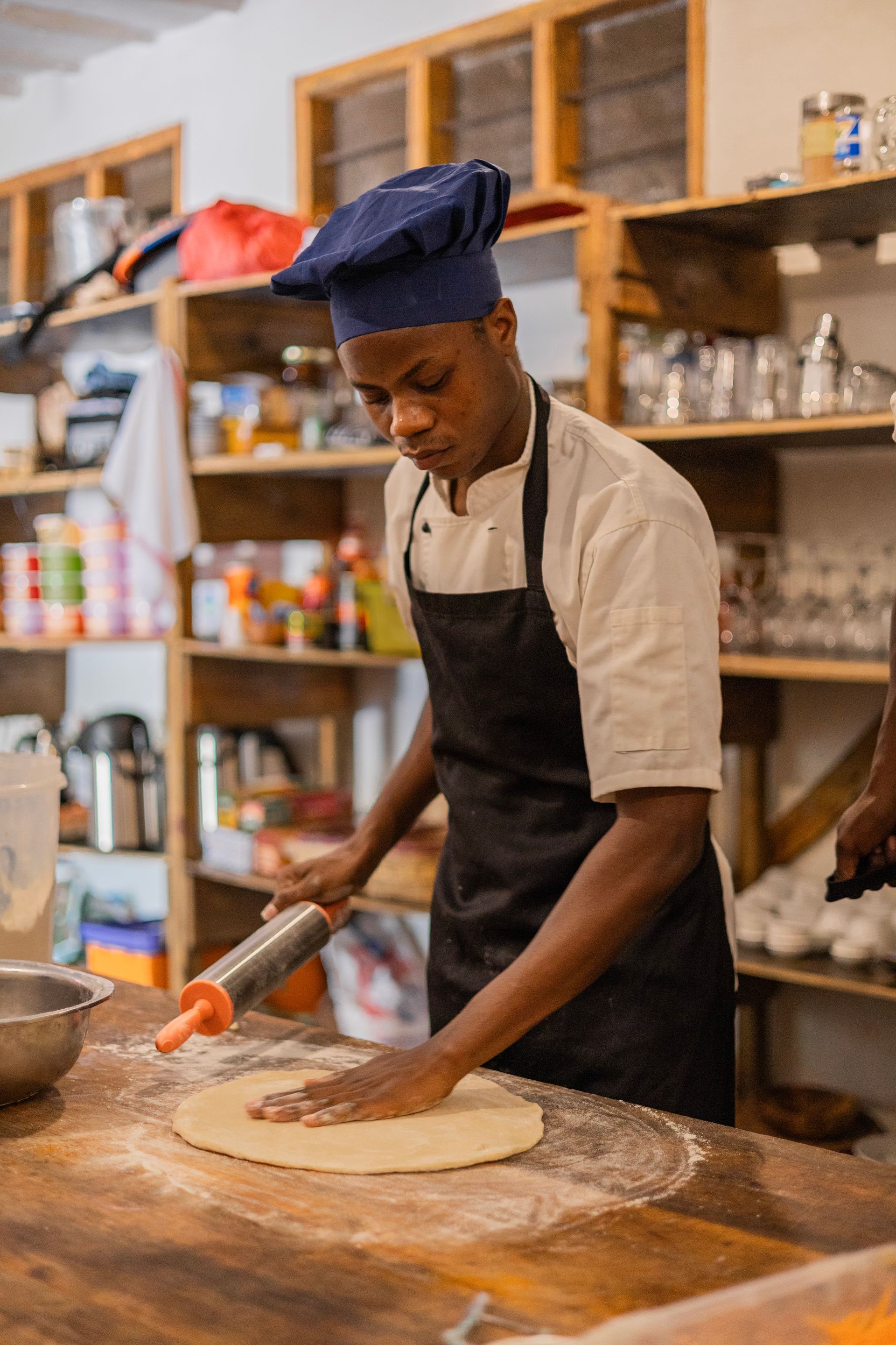 A man in a chef 's hat is rolling dough on a wooden table.