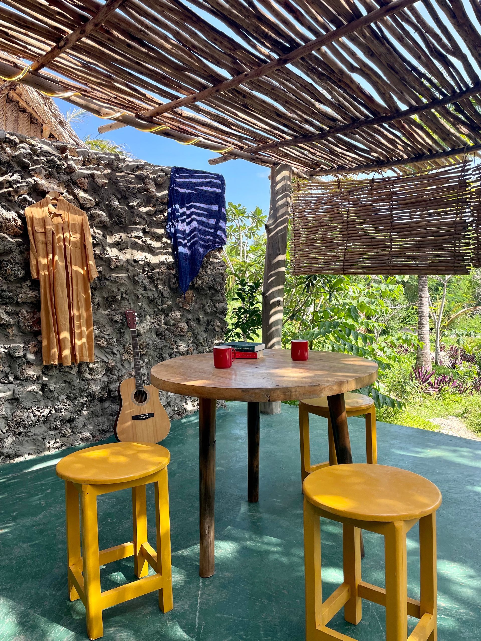 A wooden table with yellow stools under a bamboo canopy.