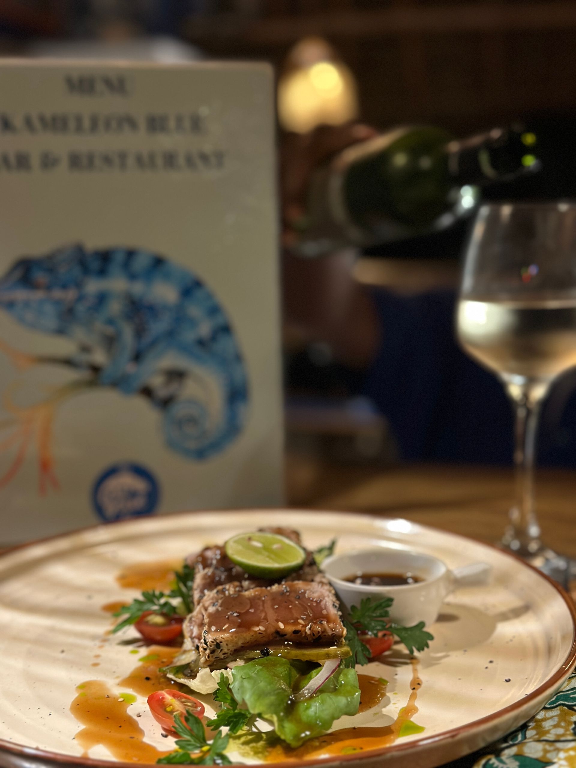 Plate of food with lime, glass of white wine, restaurant menu in background.