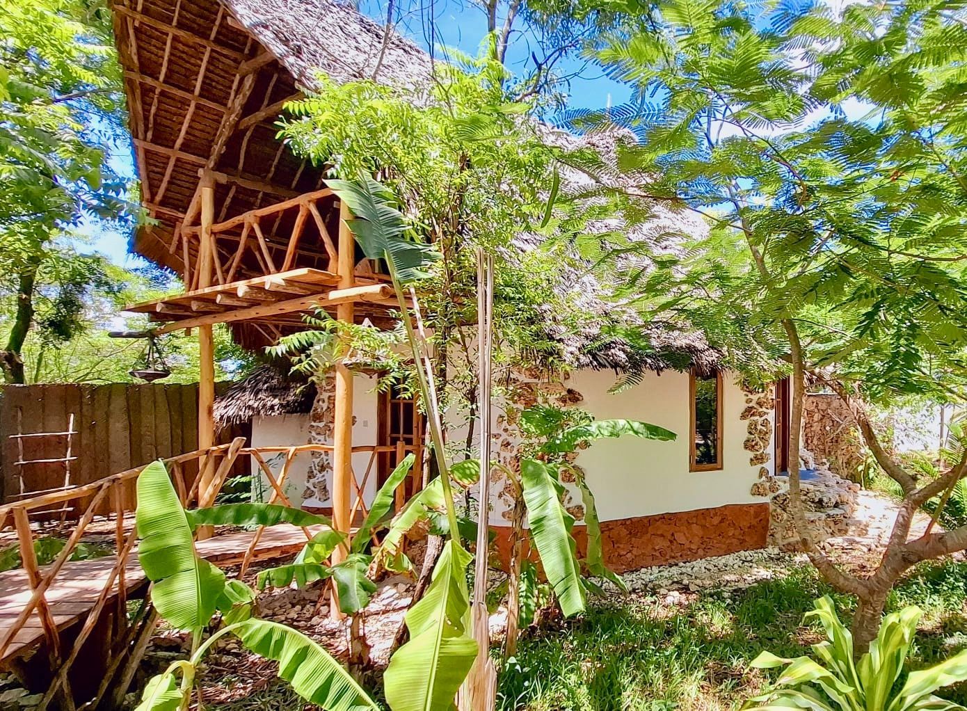 A wooden tropical bungalow with a thatched roof surrounded by lush greenery.