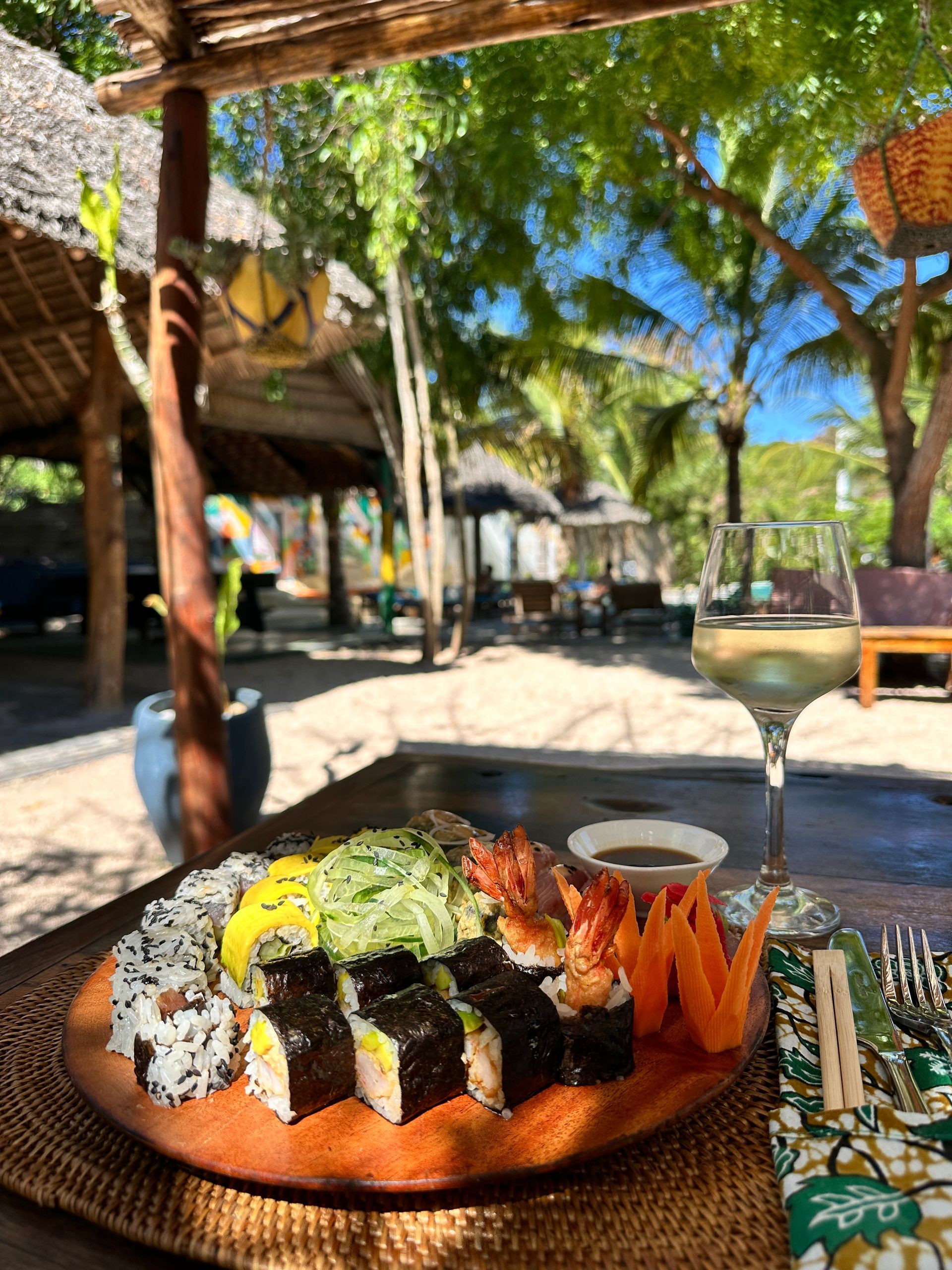 Sushi plate and wine glass on a table with tropical outdoor background.