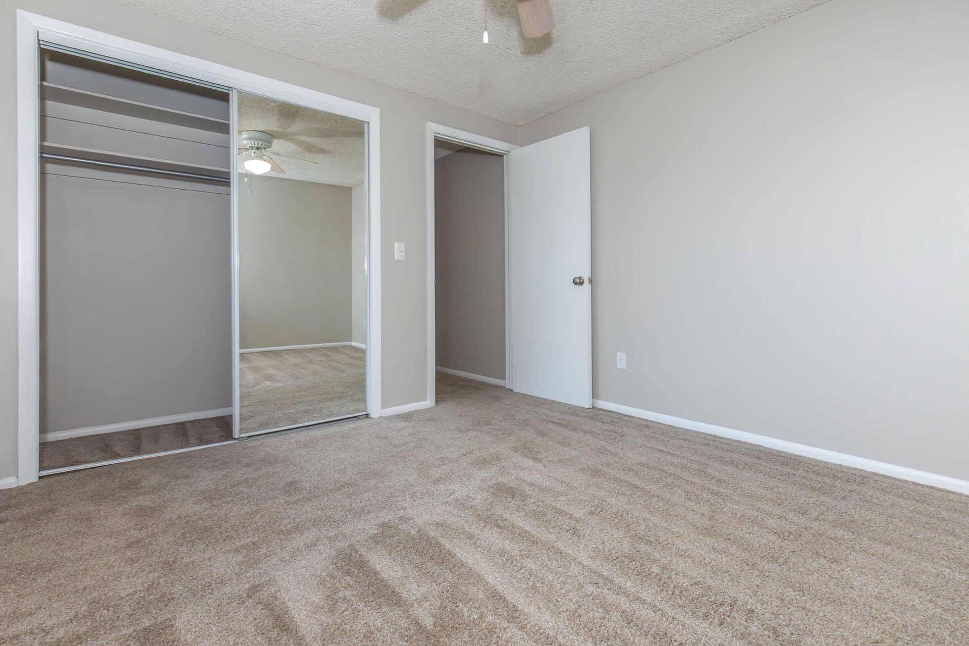Empty bedroom with beige carpet, mirrored closet doors, and a closed white door.