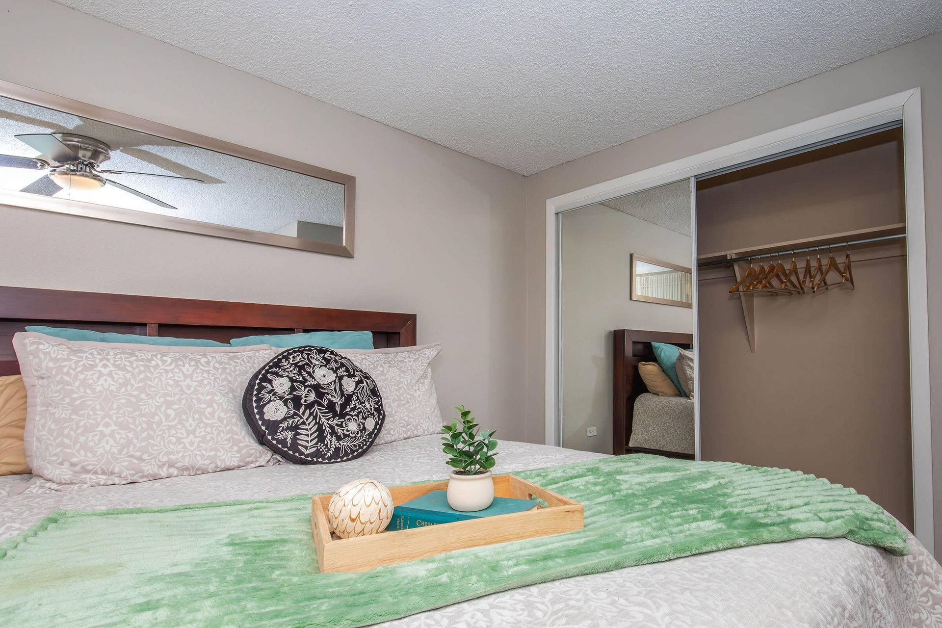 Bedroom with bed, closet, and decor. Bed has green blanket and pillows. Light brown walls and ceiling.