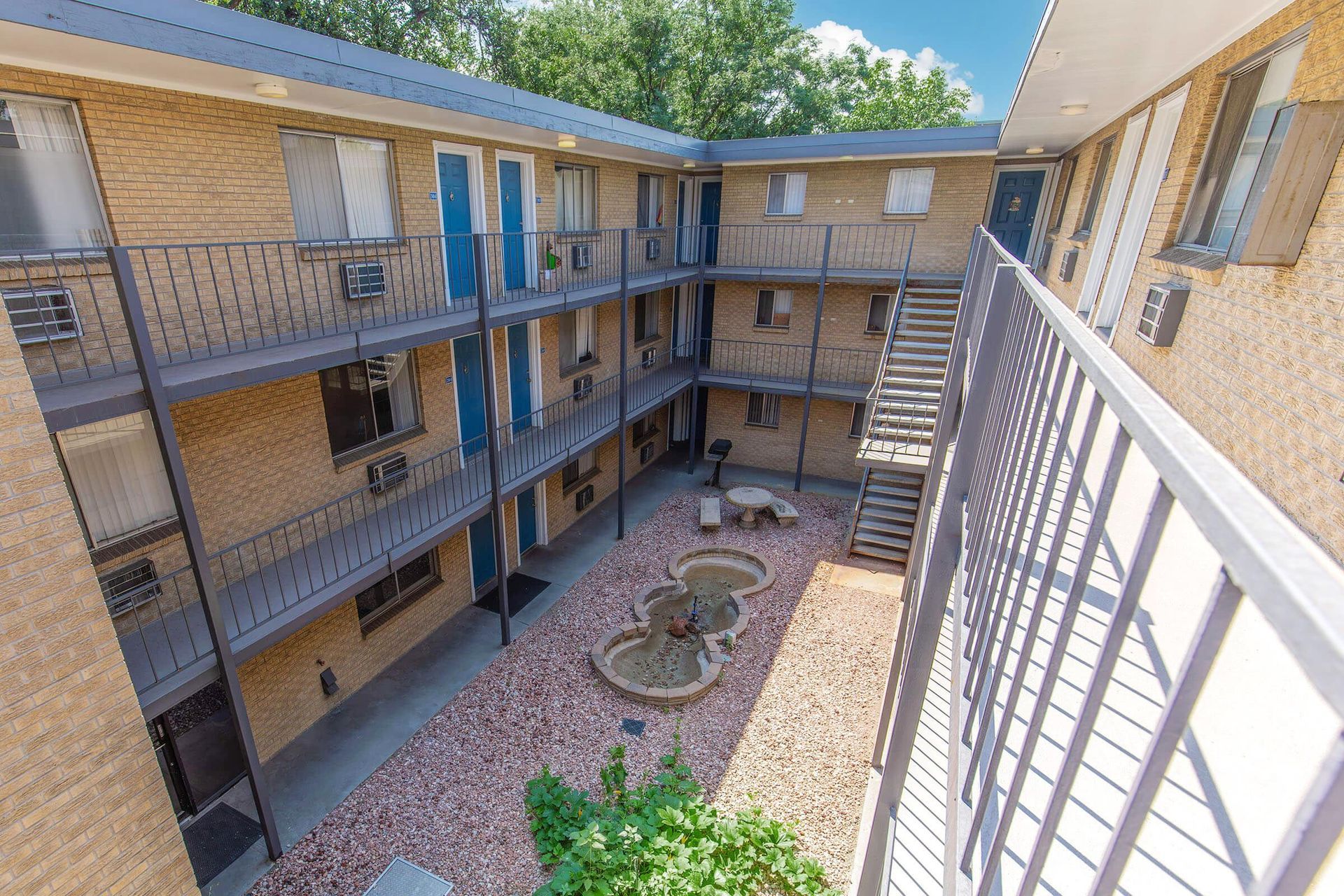 Courtyard apartment building with three levels, brick exterior, and metal balconies.