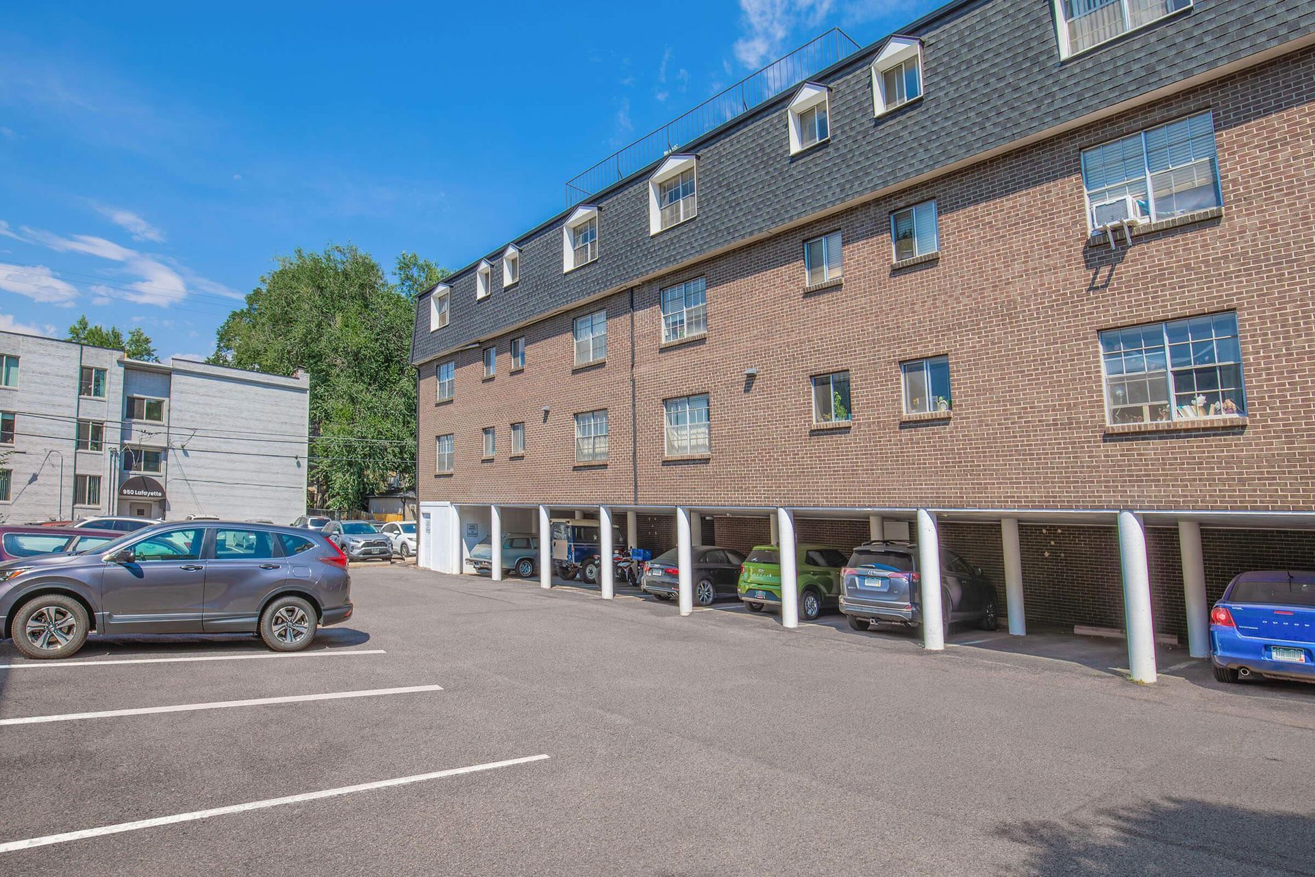 Multi-story brick apartment building with covered parking underneath and a parking lot.