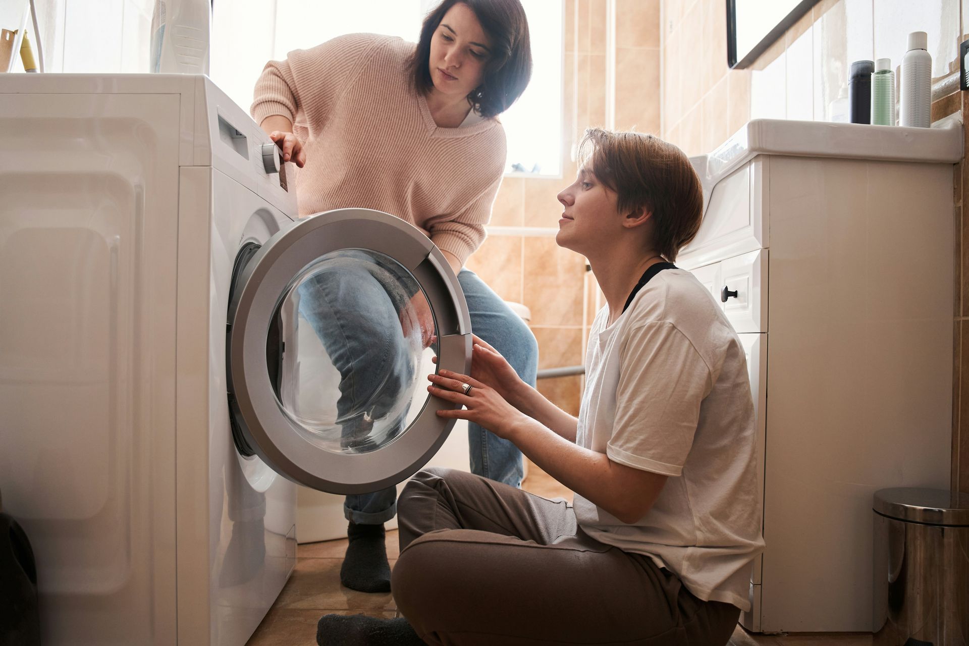 Two people loading laundry into a front-loading washing machine in a bright laundry room