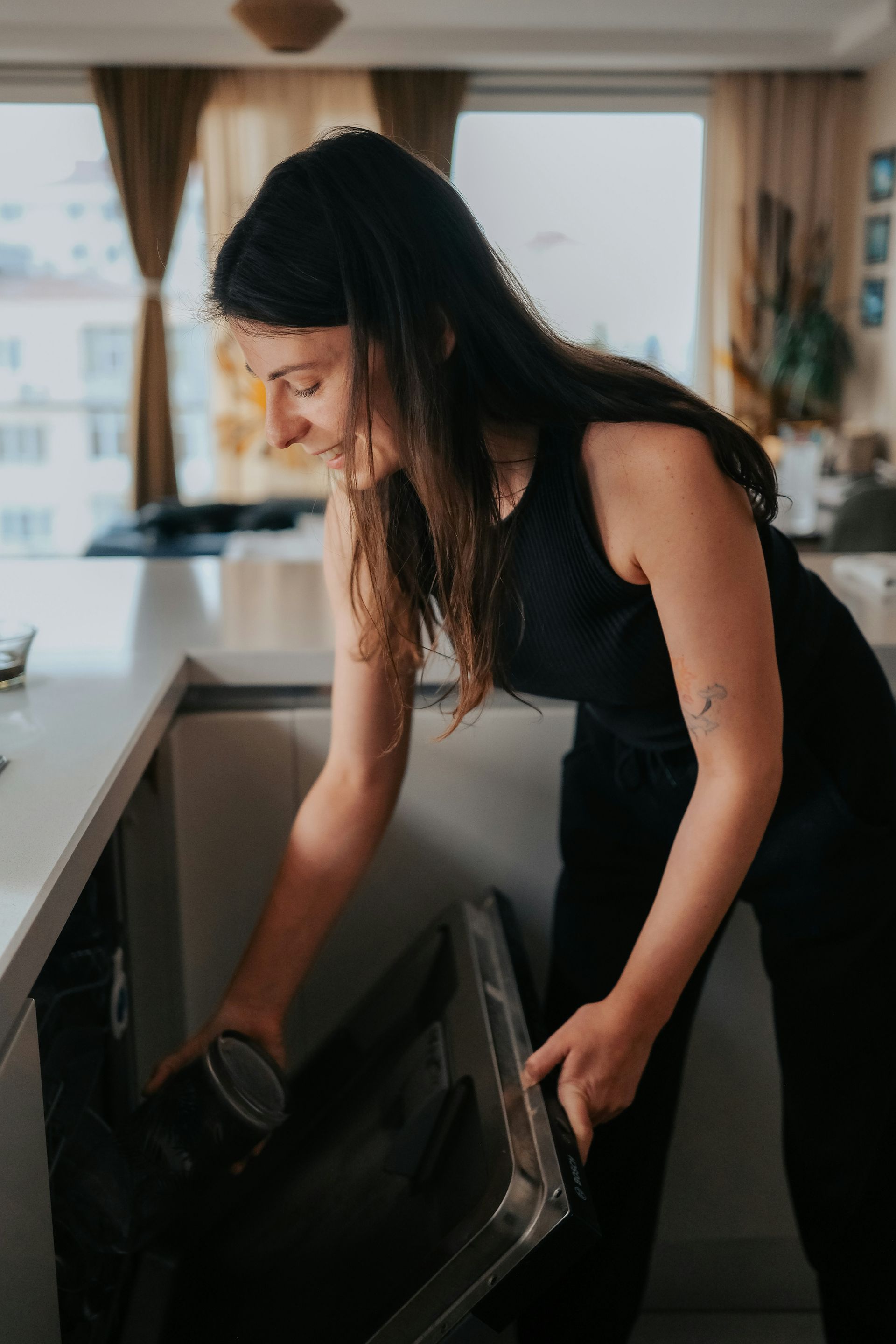 Person loading a black appliance in a bright kitchen with large windows