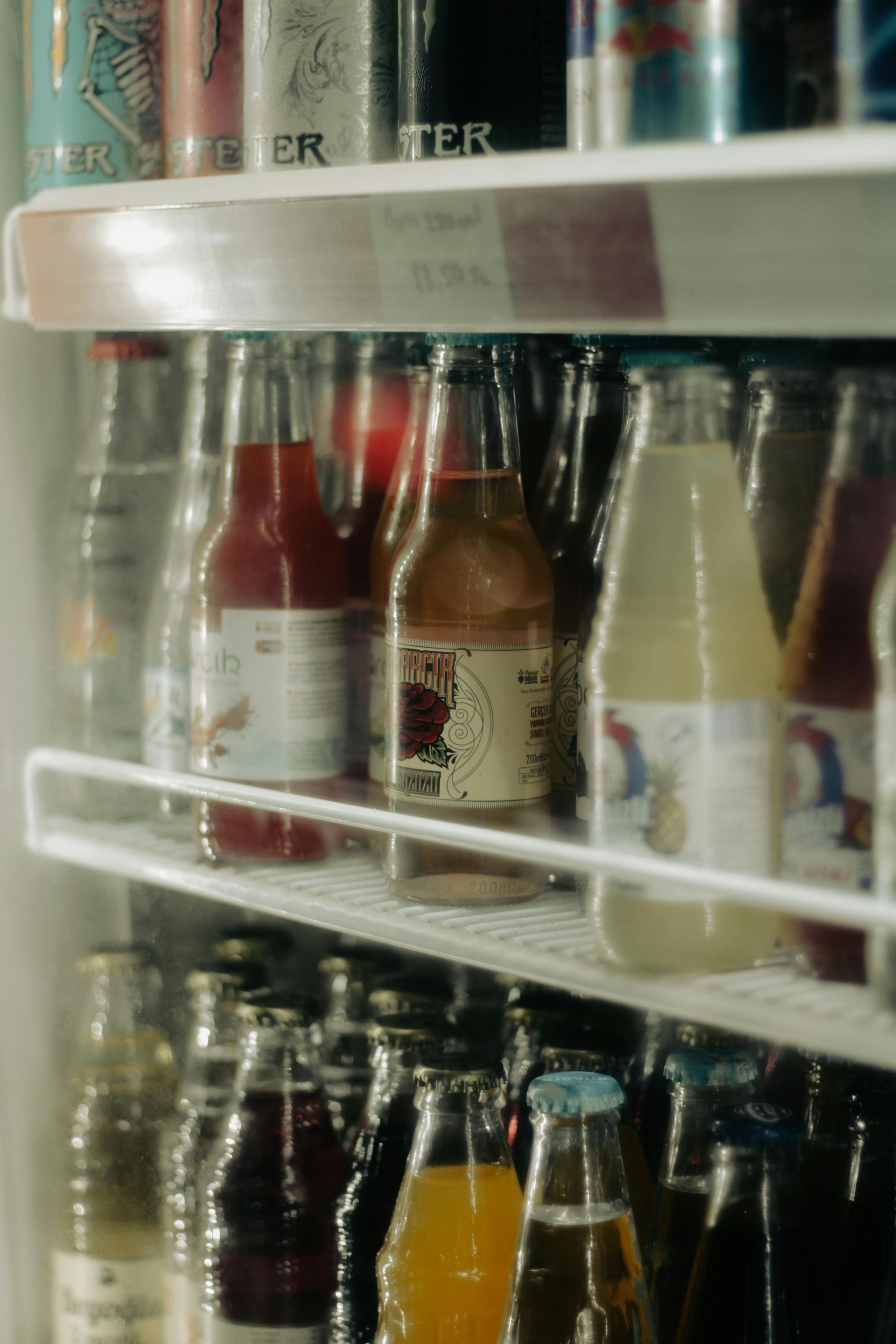 Assorted bottled drinks on a store shelf, including red, orange, and clear beverages in white wire racks.