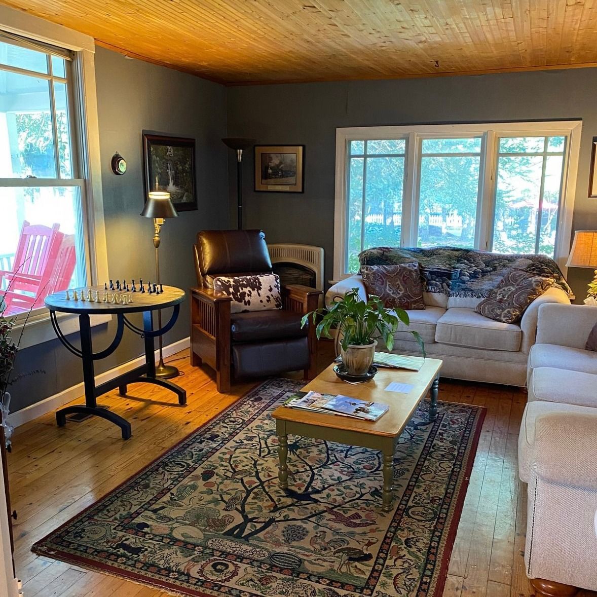 Cozy living room with wood ceiling, dark gray walls, light-colored sofa, floral rug, and a chess set on a small table.