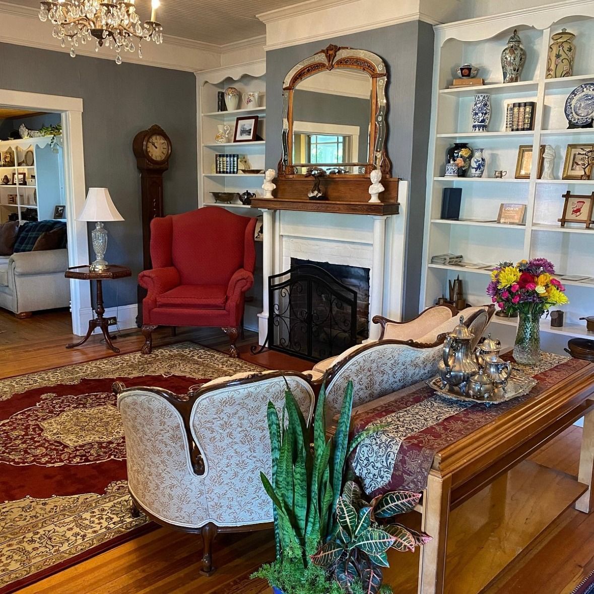 A traditional living room with a red rug, fireplace, sofa, and bookshelves filled with decor.