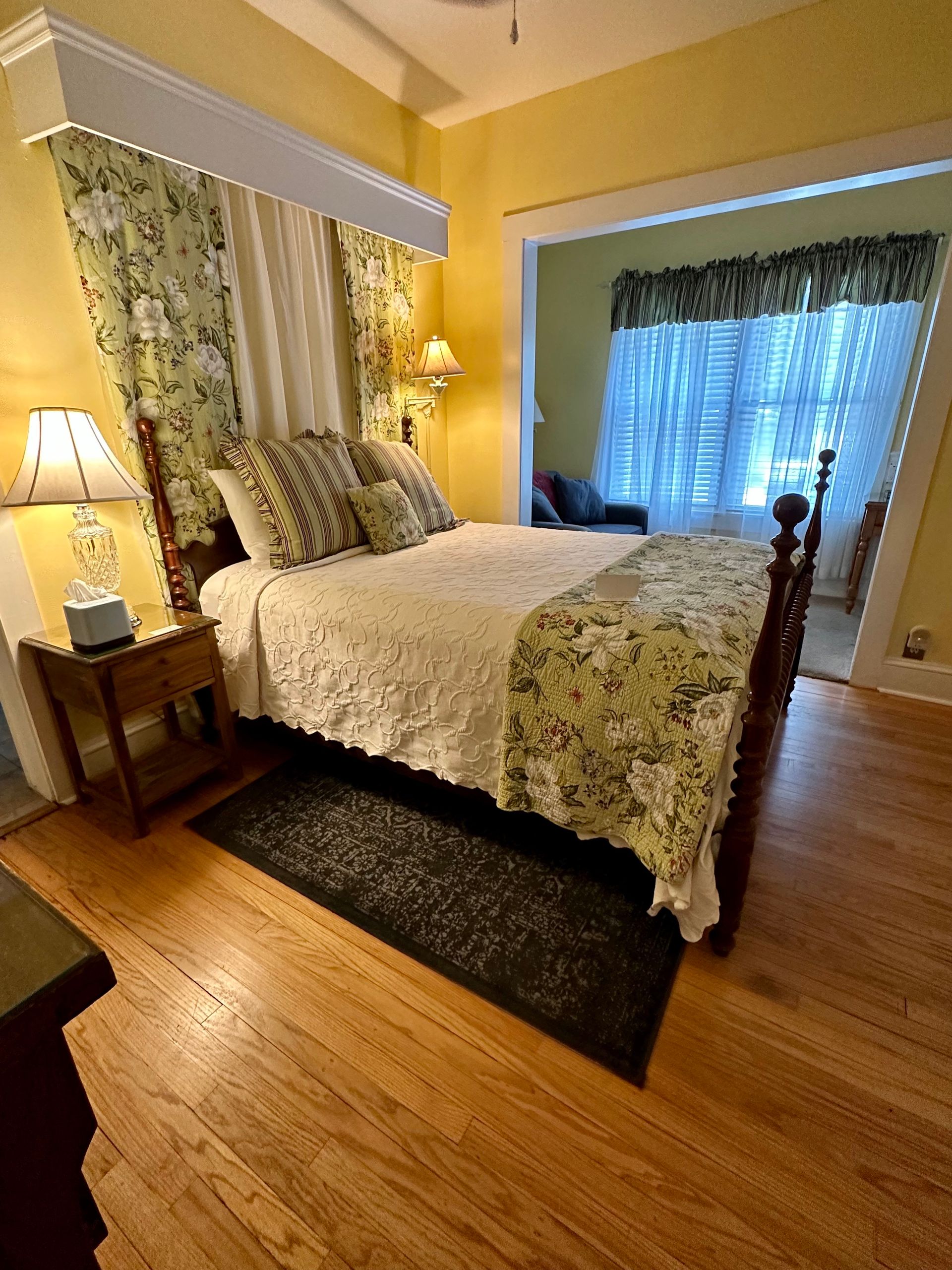 Bedroom with a wooden bed, white bedspread, and green floral accents. 