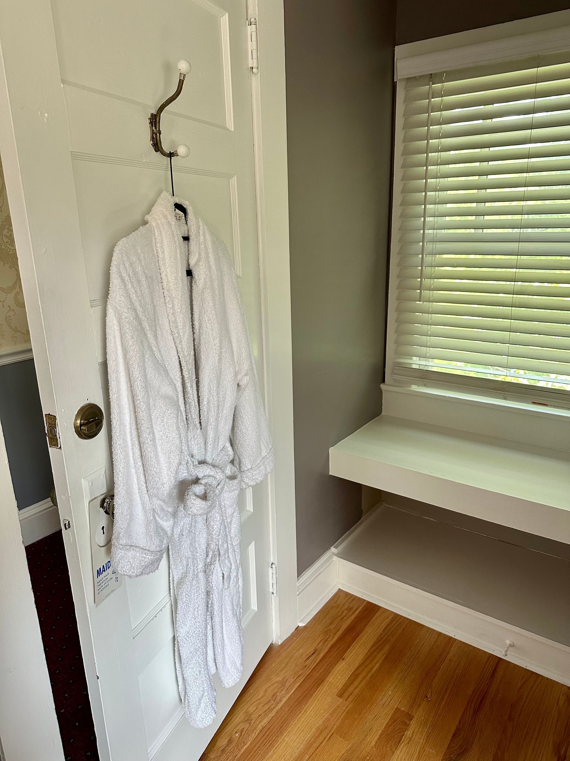 White bathrobe hanging on a hook on a white door. 