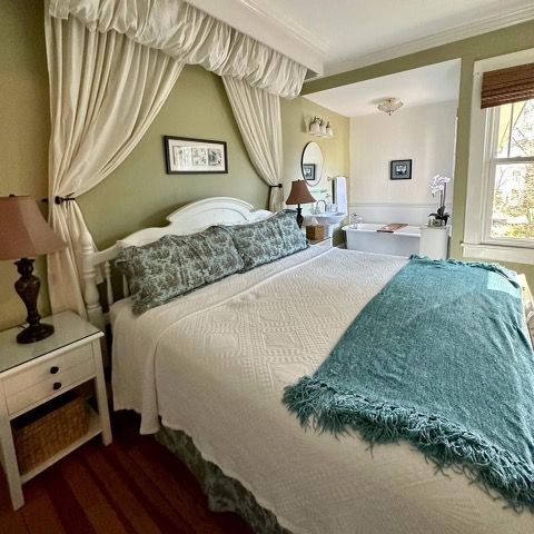 Cozy bedroom with a draped canopy bed, a nightstand, and an en-suite bathroom. 