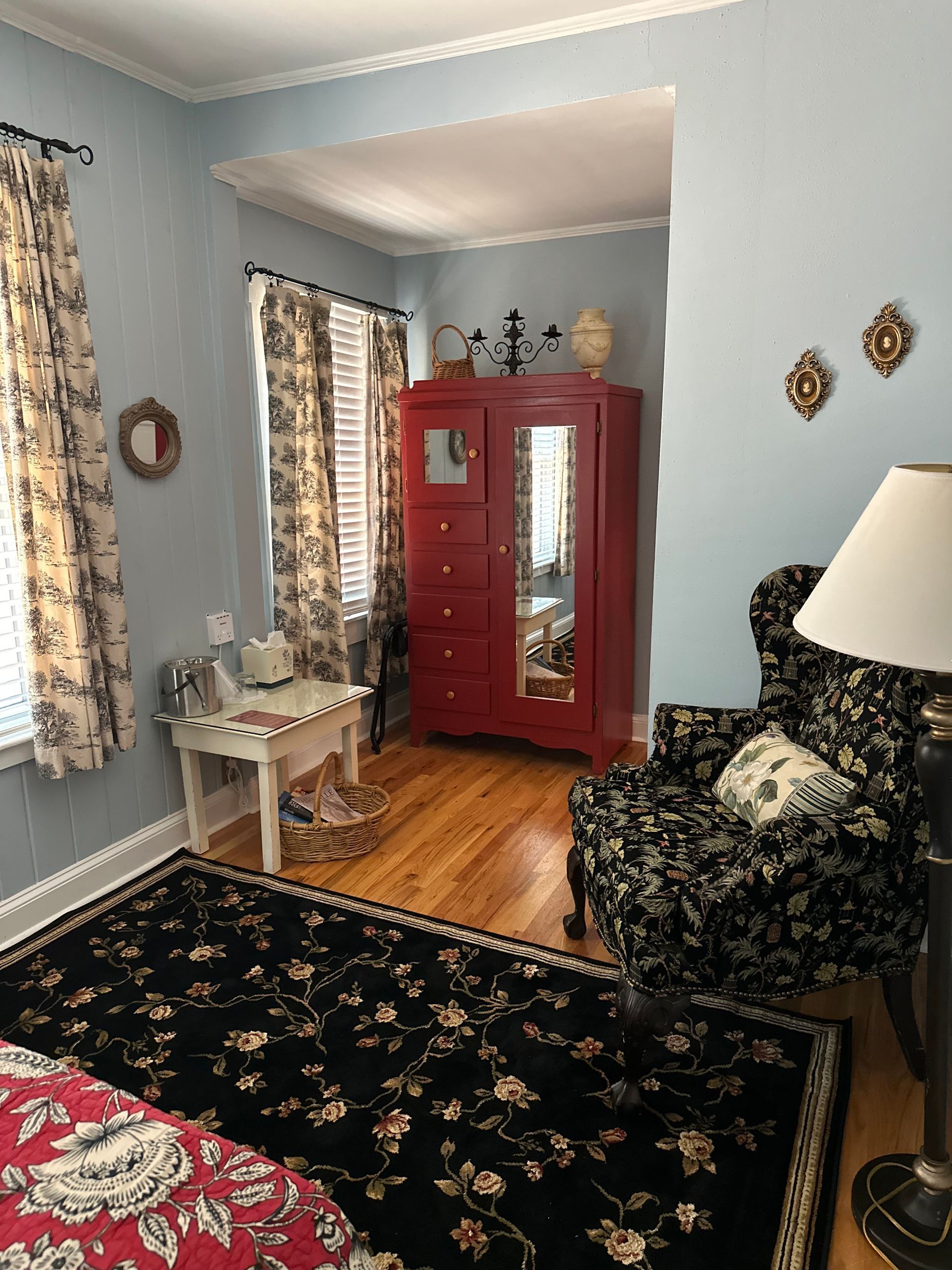Bedroom with red floral bedspread and rug. A red wardrobe and blue walls are also visible.