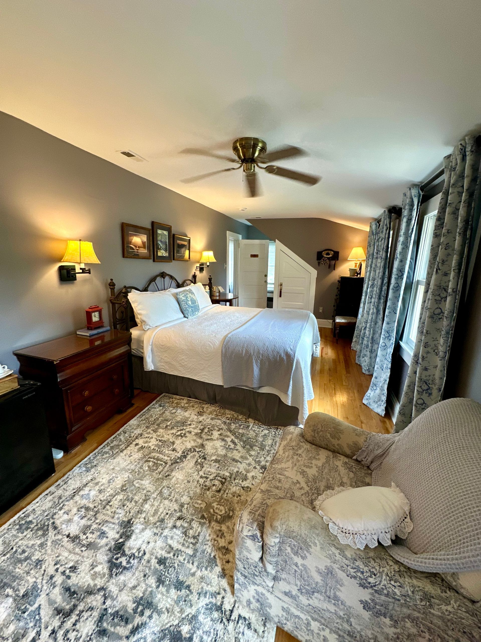 Cozy bedroom with wooden floor, bed, armchair, and coffee station. 