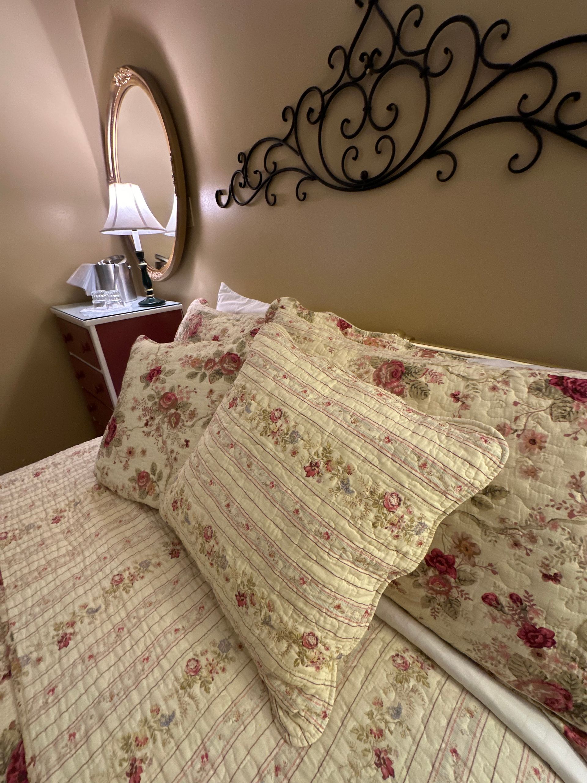 A bedroom with a bed, a partly open door to a bathroom, and artwork on the wall. Warm yellow tones.