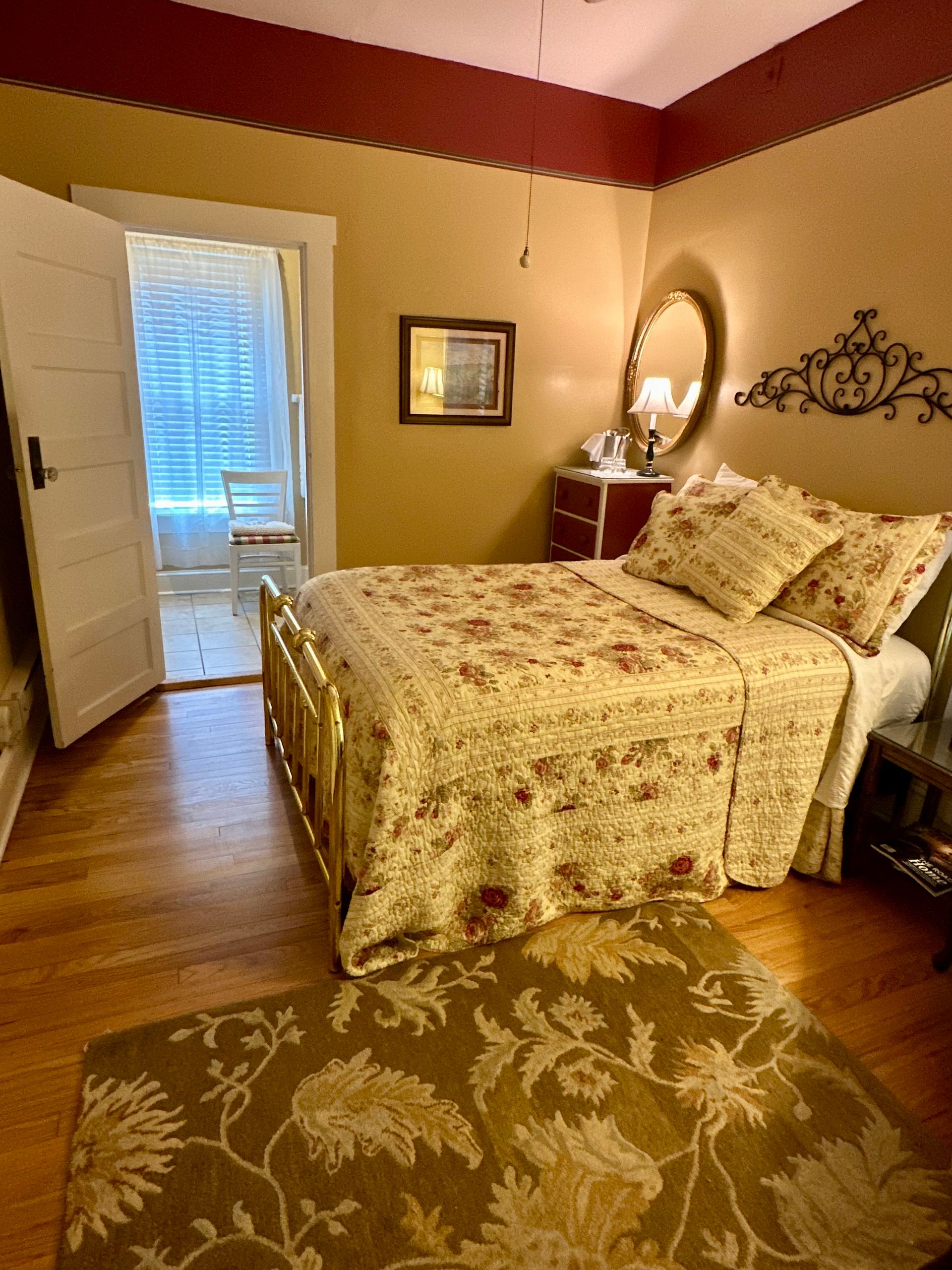 Bedroom with vintage-style bed and floral patterned quilt, rug, and headboard decoration. Room has red and cream walls.